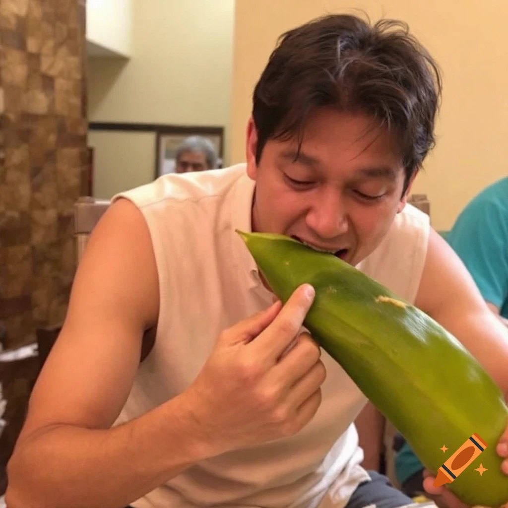 A man bites into a large green leaf while holding it with both hands. Another person is blurred in the background.