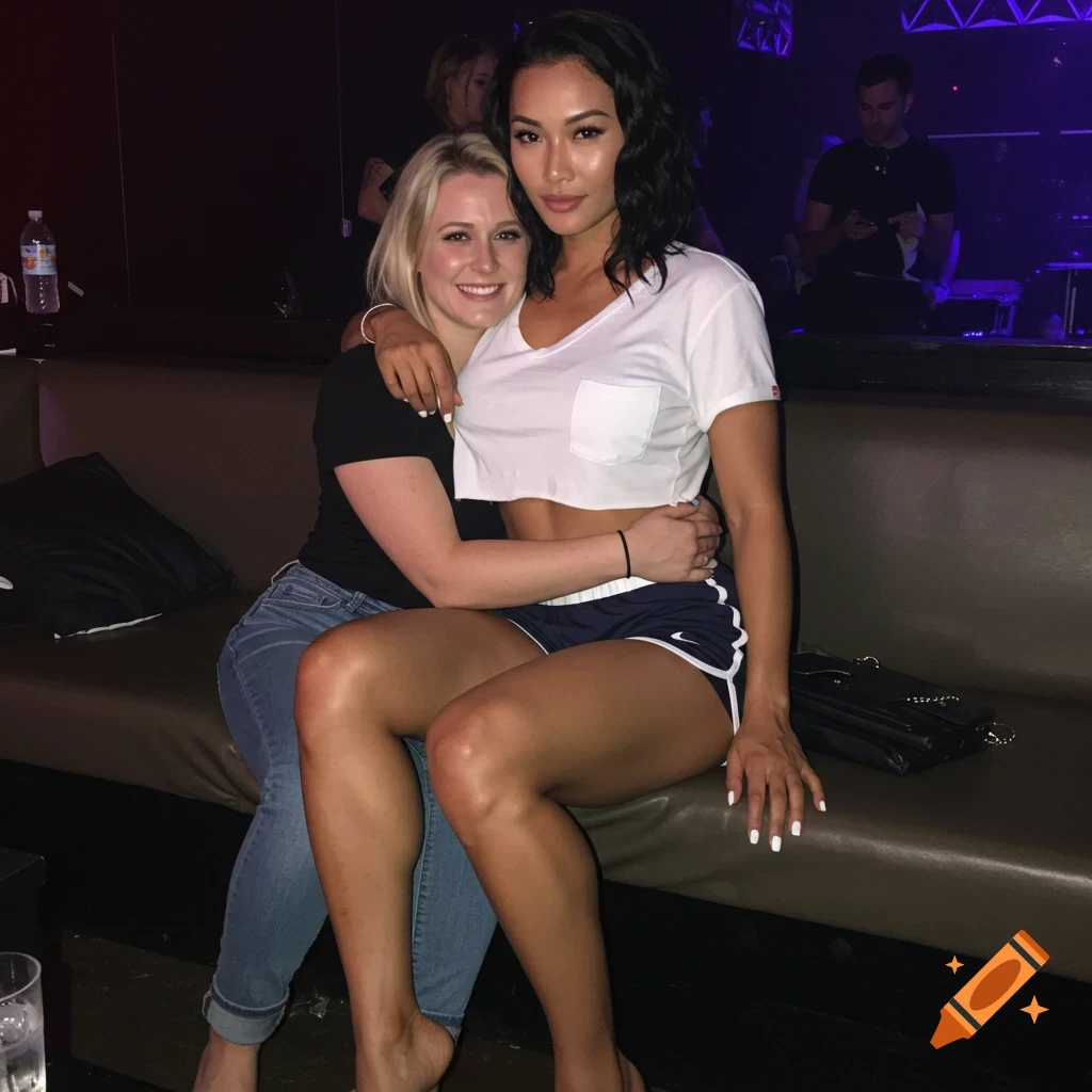 Two women hug while sitting on a couch in a dark nightclub.