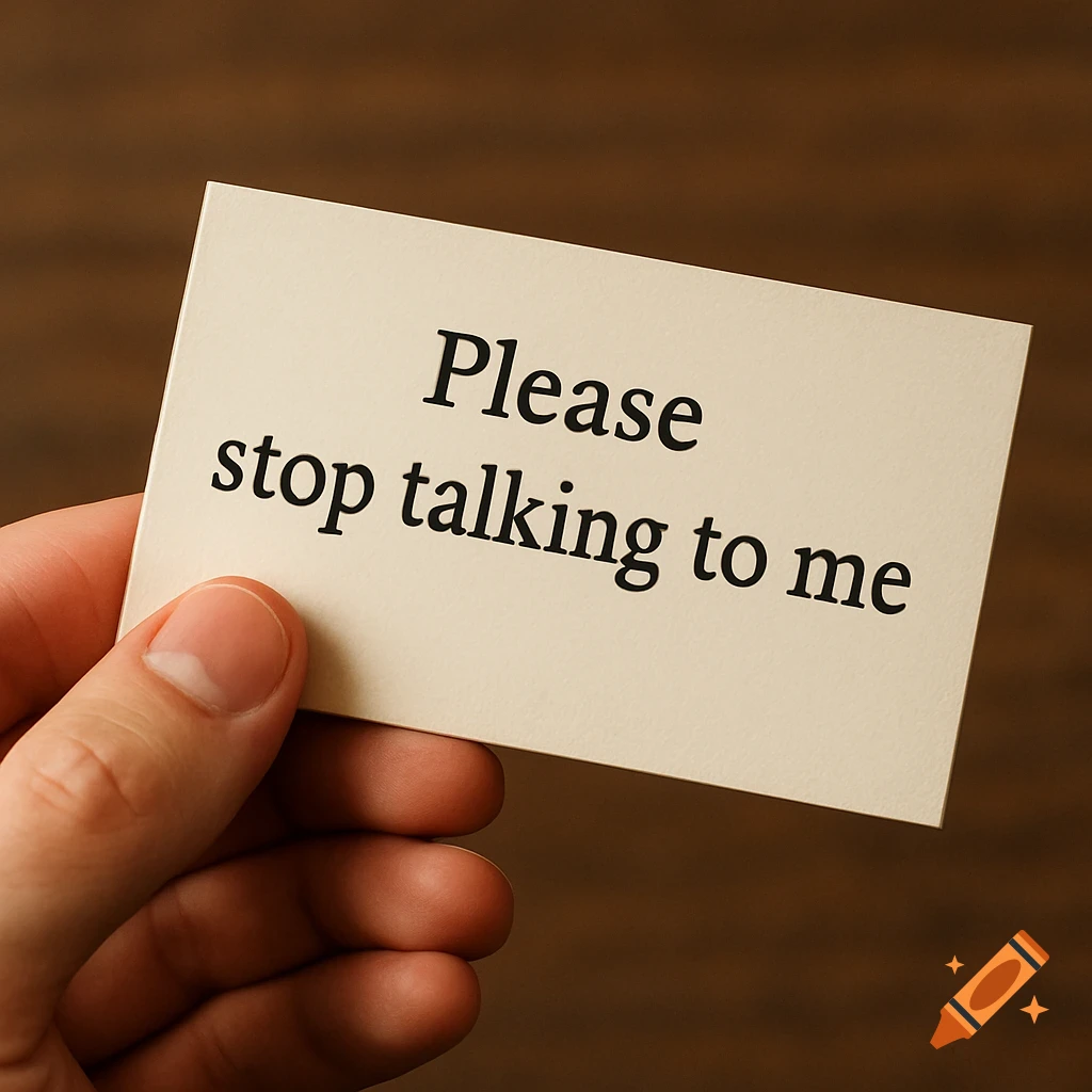 A hand holds a beige business card that reads "Please stop talking to me." on a wooden background.