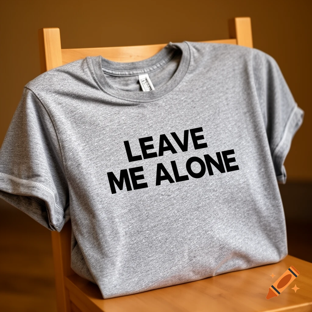 Grey t-shirt with 'LEAVE ME ALONE' in black text, folded on a wooden chair.
