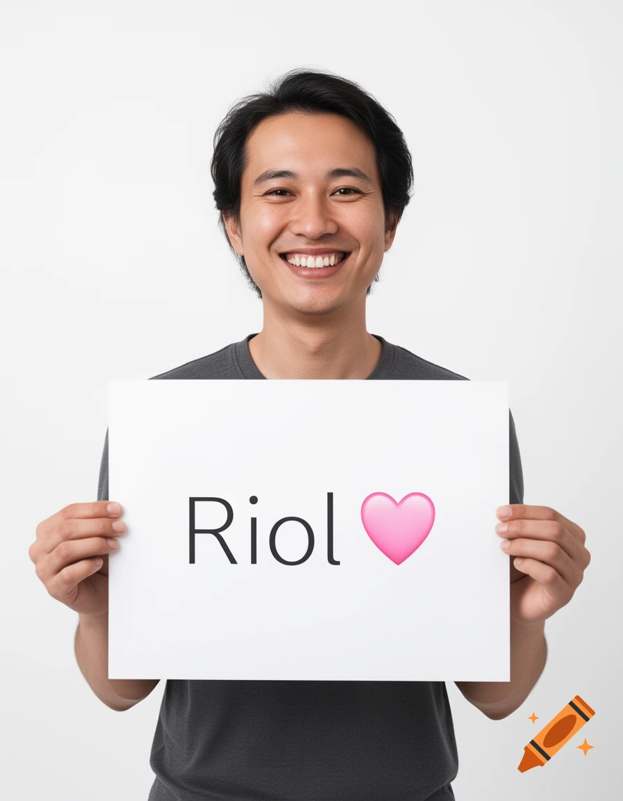 A smiling man with dark hair holds a white poster board displaying the word "Riol" followed by a pink heart emoji.