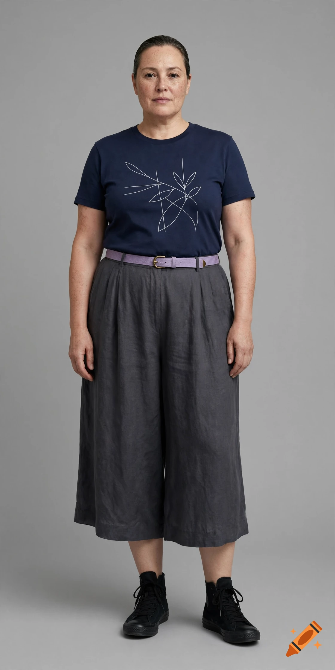 Full-body studio photograph of a middle-aged gender-neutral person wearing a navy graphic t-shirt, charcoal culottes, and black high-tops.