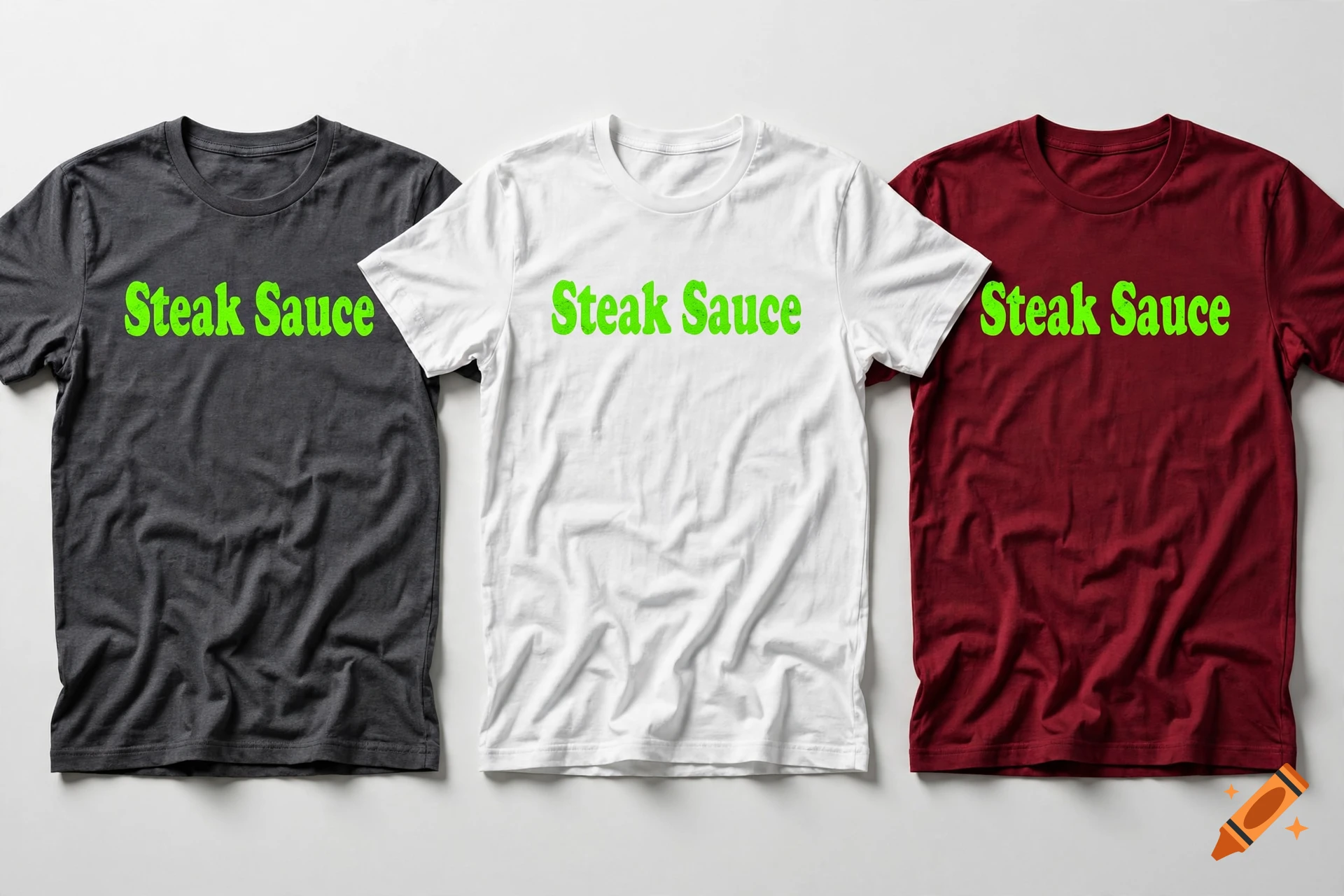 Three folded t-shirts in dark grey, white, and burgundy, each with neon green 'Steak Sauce' text.
